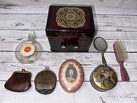 Arrangement of vintage Bakelite makeup box, powder boxes, hairbrush, mirror, small perfume bottle and coin purses on wood surface