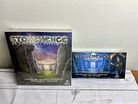 Photo showing Stonehenge - An Anthology Board Game box and Stonehenge Nocturne Expansion box side by side on a white wood surface.
