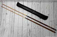 Overview of two vintage wooden pool cues alongside a black soft carrying case on wood plank floor background.