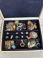 Overview of assorted vintage costume jewelry displayed in a black lined case with compartments showing necklaces, bracelets, earrings, rings, brooch and pendants.
