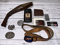 Photo showing all items in the lot including five belt buckles, two wallets, two leather belts, and a packaged Harley Davidson towel.