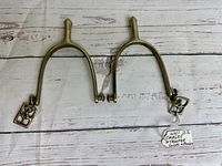 Pair of metal cavalry trooper spurs on white wood background with label tag showing 'WWI U.S. Cavalry Trooper Spurs w/ Buckles'