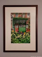 Framed watercolor painting showing an outdoor porch scene with greenery and flowers, well-lit and mounted on a light wall.