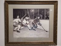 Framed black and white photo of three NHL legends on ice with audience in background