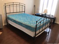 Full side and corner view of assembled metal bed frame with mattress and box spring in bedroom area.
