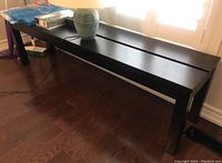 Full view of wood frame bench with dark wood laminate top, placed on hardwood floor with items on top