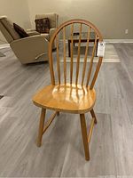 Side and front view of a wooden chair with arched dowel backrest and smooth wood seat on angled legs with stretchers.