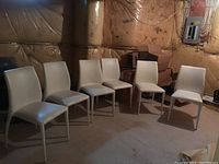 Six metal frame chairs with light-colored vinyl padded seats and backs arranged in a row showing front and side views.