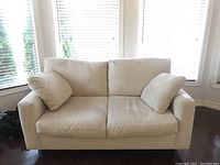 Front view of the Better By Design loveseat sofa couch showing beige fabric upholstery, two seat cushions, and two matching pillows.