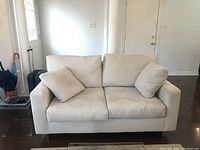 Full front view of beige loveseat couch against white wall and door background with two cushions on seat.