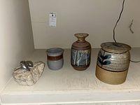 Metal figure with abstract form mounted on natural stone base alongside three pottery vessels with distinct designs and glazes.