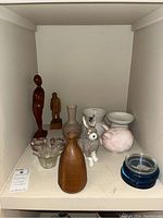 Wood statues, ceramic and glass vases, ceramic piggy bank, animal figurines, glass candle holders, and blue glass coasters displayed on a shelf.
