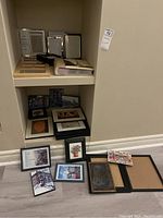 Two shelves with various photo frames, some stacked and some standing, along with scattered albums on the floor