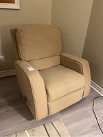 Front-left angle view of beige Lazboy reclining armchair with fabric upholstery, showing armrest, seat cushion and back support in room corner.