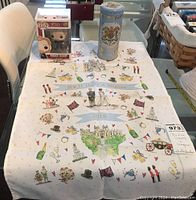 Photo showing all three items: Prince Harry Funko Pop box, folded tea towel with royal wedding-themed prints, and decorative Buckingham Palace tin.