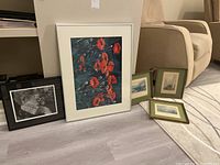 Five framed prints arranged on floor near wall and chair, showing size variation and frame styles