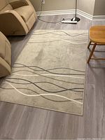 Area rug on floor with beige background and wavy lines in beige, taupe, and gray tones, showing some dirt and marks.