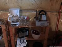 Photo showing all items on a wooden shelf rack: coffee maker, kettle on box, glass jars, vegetable mill, deep fryer, mixing bowl, and red cutter.