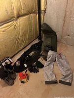 Photo showing snowboard boots, black snowboard helmet, gloves, green knit hat, orange accessory, two green bags, and white Sunice snow pants.