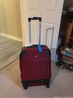 Full view of the red Swiss Gear suitcase with four wheels and luggage tag, standing upright with extended handle.