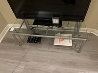Full view of the tempered glass and metal TV stand under a flat-screen TV, showing glass shelves and metal frame.