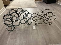 Two metal wine racks on a wood floor, showing their designs side by side.