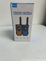 Front view of NXGKET walkie talkies box showing both devices in orange and blue with antennas and display screens.