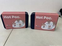 Two Hot Poc hand warmer tin boxes side by side on a white surface.
