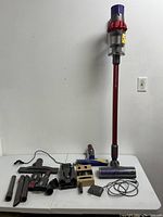 Multiple Dyson vacuum parts and accessories laid out including main unit, attachments, charger