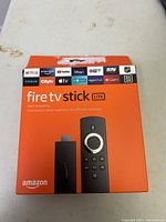 Front view of orange Amazon Fire TV Stick Lite box showing device and remote image and streaming service logos.