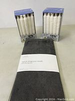 Two boxes of 20 IKEA Jubla white long stick candles each, stacked vertical, with a dark gray Maison Simons dish drying mat in original packaging