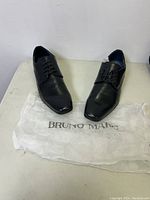 Pair of men's black Bruno Marc dress shoes on a table with Bruno Marc branded paper.