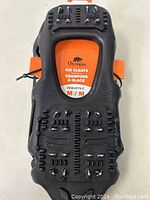 Top view of black Olympia ice cleats showing rubber base with embedded metal microspikes and size labeling.