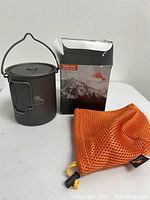 TOAKS titanium pot with bail handle, orange mesh bag and original box grouped on white surface.