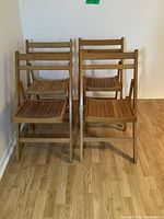 Front view of all four vintage wooden folding chairs, showing slatted seats and backs, natural wood finish, and condition variation.