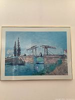 Front view of framed art print showing a river with stone drawbridge, water, and trees under blue sky.