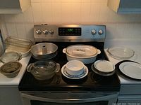 Wide shot of all kitchenware items arranged on white countertop including glass baking dishes, mixing bowls, metal tube cake pan, plastic container, and dinner plates.