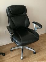 Front and angled views of a black vinyl office chair, showing padded seat, backrest, and armrests with silver five-wheel base.
