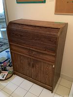 Front view of wooden roll top table with closed tambour cover and lower cabinet doors visible.