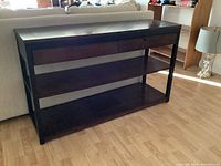 Front view of the wooden console table showing two drawers and two large shelves underneath, dark finish, placed behind a couch.
