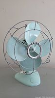 Front view of the light blue Calor electric fan showing its four blades and protective metal cage with logo center.