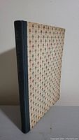 Closed book standing upright showing cover with patterned fleur-de-lis design and dark spine.