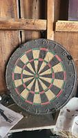 Full view of round bristle dartboard with traditional scoring colors and numbers, showing wear and placement on a wooden shelf.