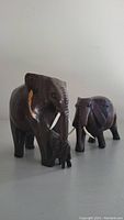 Two hardwood elephant carvings placed on a flat surface showing front and side view, tusks made from lighter wood