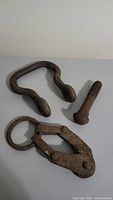 Three rusty cast iron hardware pieces on white background including hook, latch, and bolt