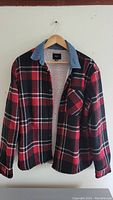 Front view of men's red and black plaid jacket with denim collar and sherpa lining hung on hanger