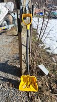 Full view of the snow shovel leaning against a post outside on gravel with snow in the background.