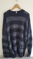 Full view of the navy blue Tommy Hilfiger sweater hanging on a wooden hanger showing horizontal patterned and solid knit stripes.