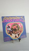 Front cover of the "The Happy Days Of Rock'n'Roll" record. Colorful 1970s style typography and artwork with musicians' images in a circular frame.