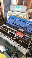 Metal toolbox open showing blue plastic tray with assorted tools and red electric drill inside